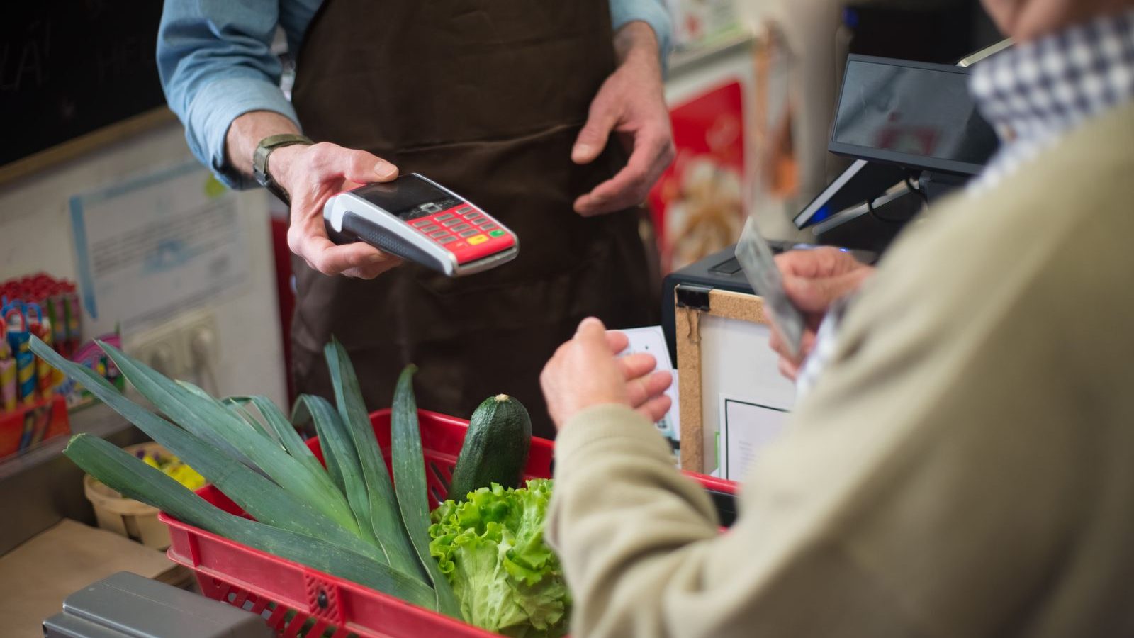 Shopkeeper taking a card payment on a handheld terminal at a grocery counter