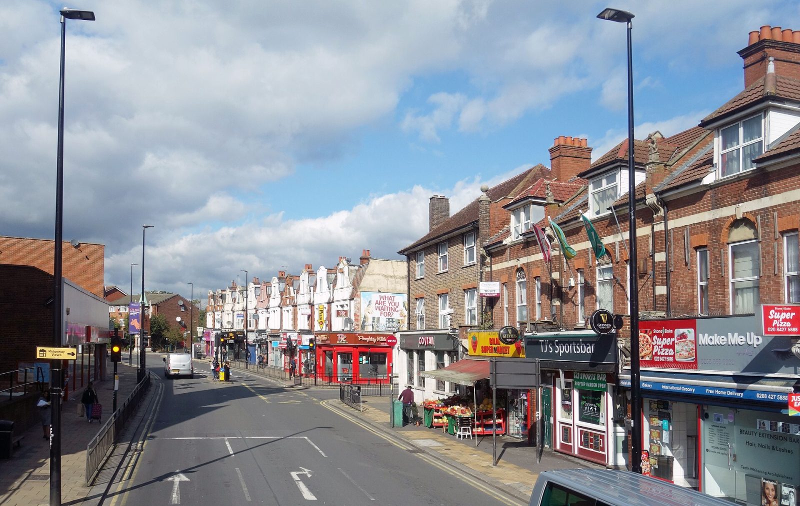 A UK high street on a sunny afternoon with independent shops, a café, a sports bar and a grocer's fruit stall